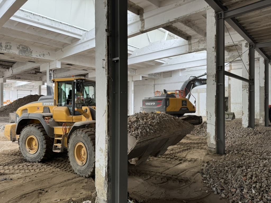 Yellow Volvo construction vehicles moving gravel inside a large unfinished building structure.