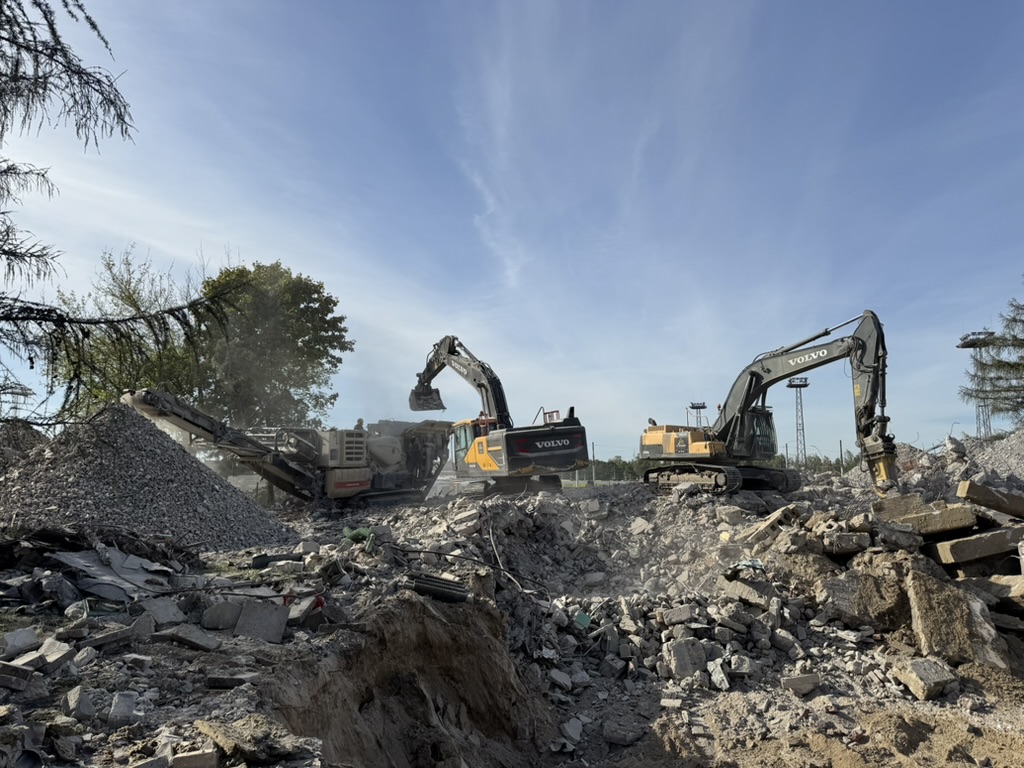 Two Volvo excavators working on rubble and debris at a demolition or construction site under blue sky.