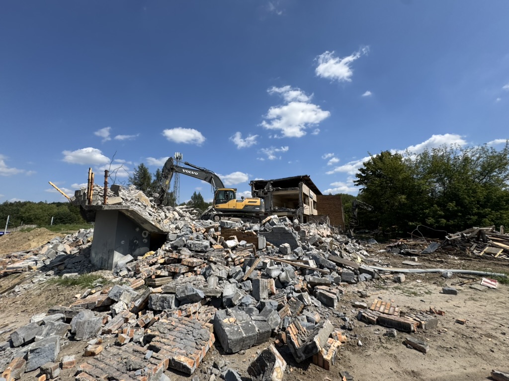 Construction excavator demolishing a building surrounded by rubble under a blue sky.