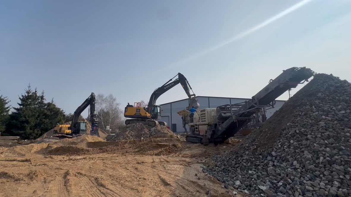 Excavators working on piles of dirt and rocks at a construction site on a clear day.