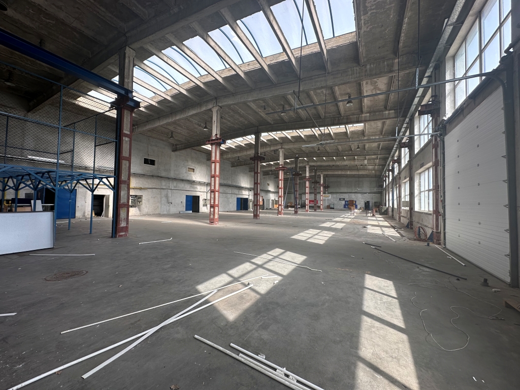 Large empty industrial warehouse with concrete floor, red support pillars, and skylights casting shadows.