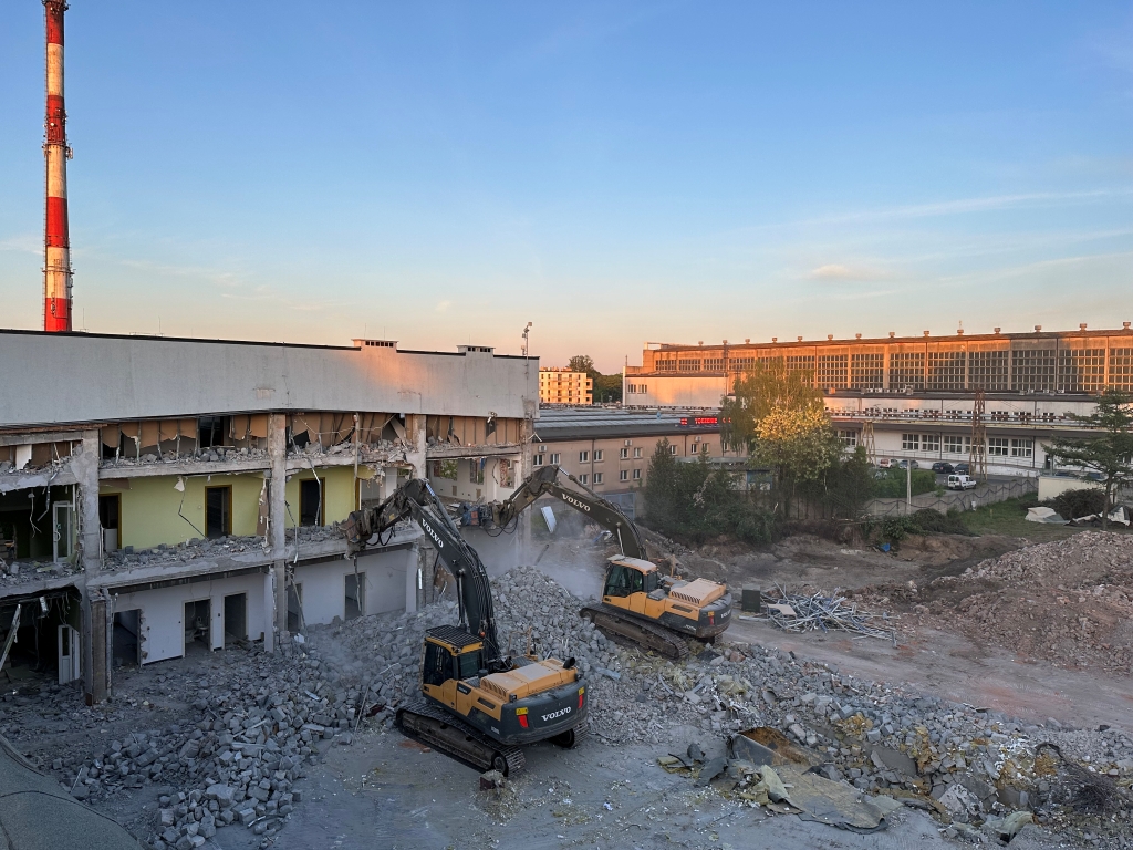 Two excavators demolishing a large building amid rubble at sunset in an urban area.