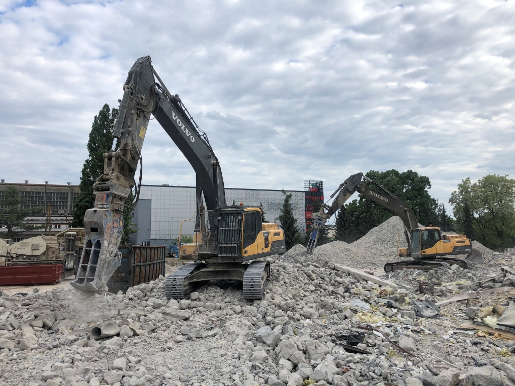 Two Volvo excavators breaking concrete rubble on a construction demolition site under a cloudy sky.