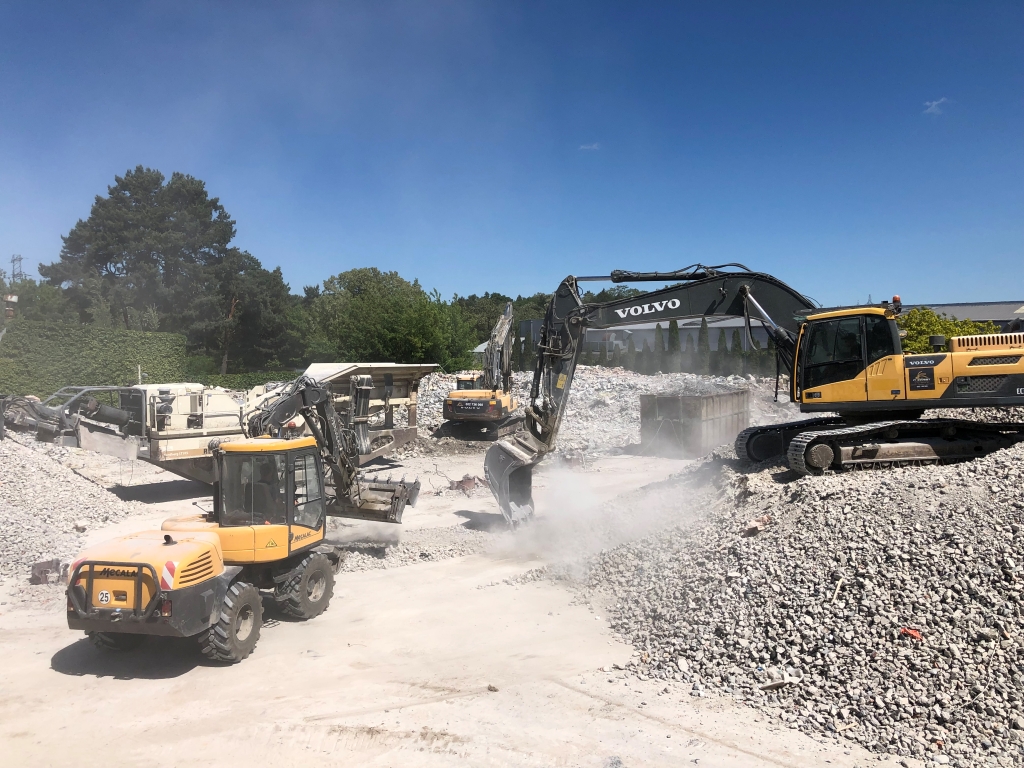 Construction site with three excavators moving gravel and rubble under a clear blue sky.