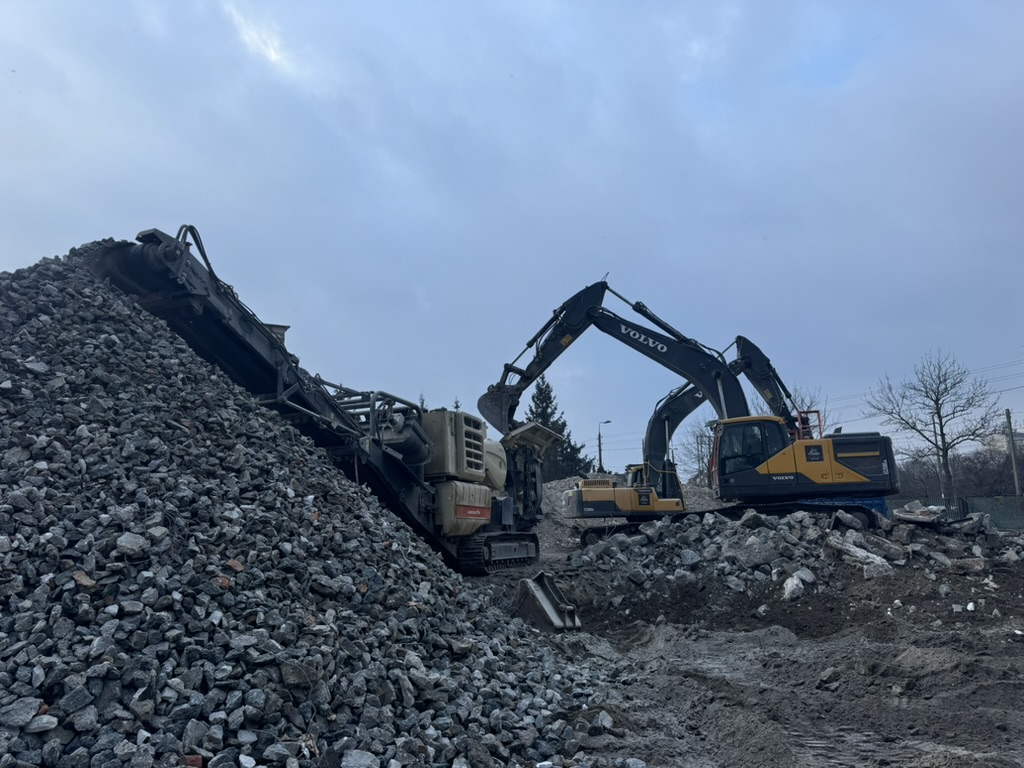 Two Volvo excavators working on rocky construction site under a cloudy sky.