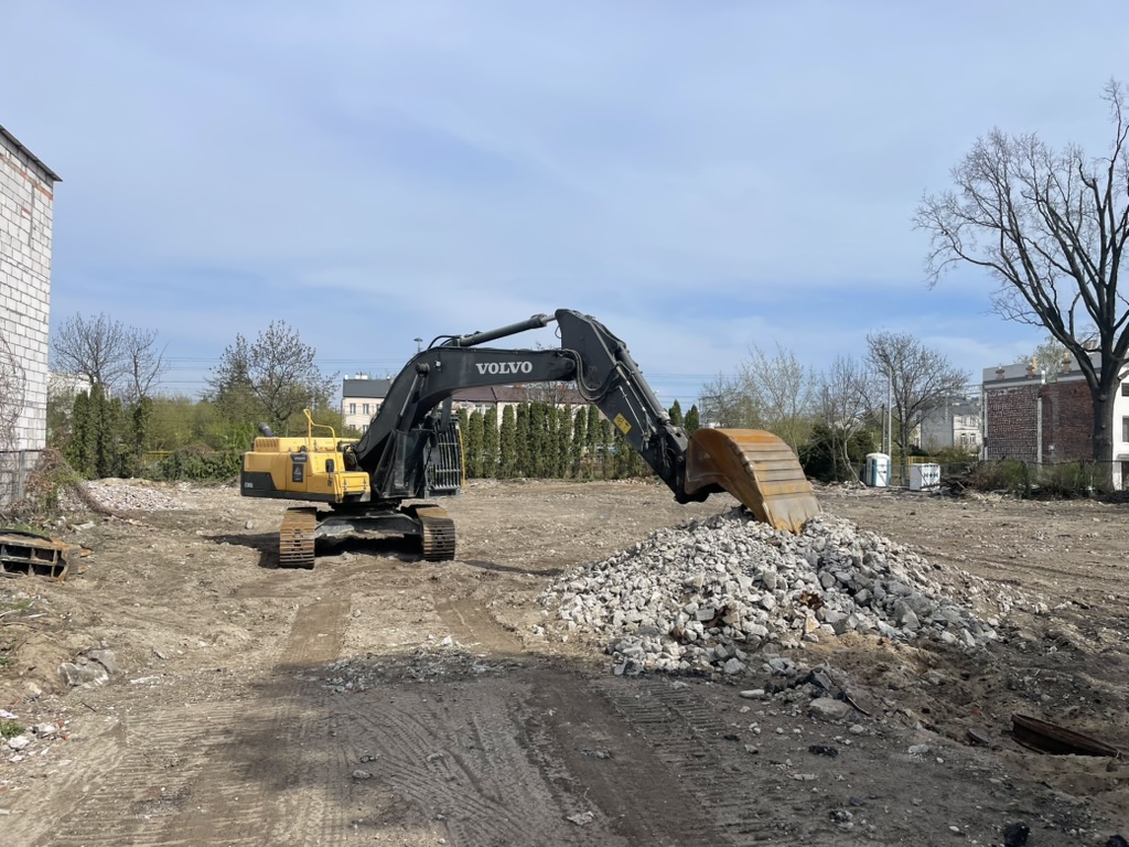 Volvo excavator with a bucket on a dirt lot, scooping a pile of rubble under a blue sky.