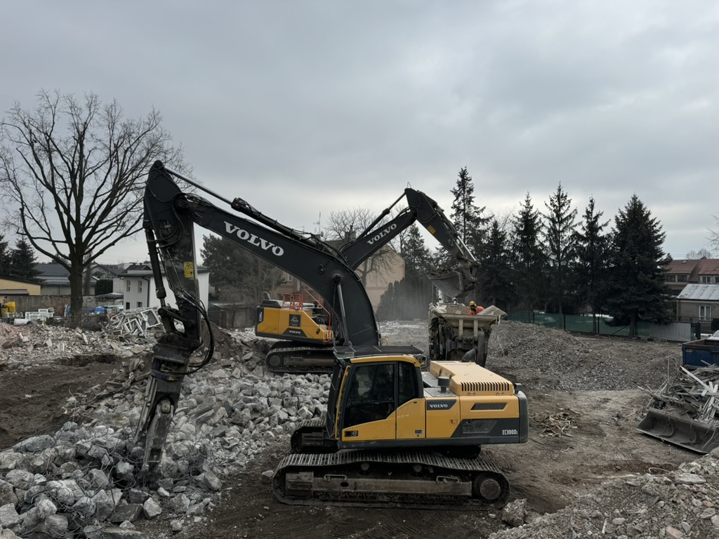 Two Volvo excavators working on rubble at a construction site under a cloudy sky.