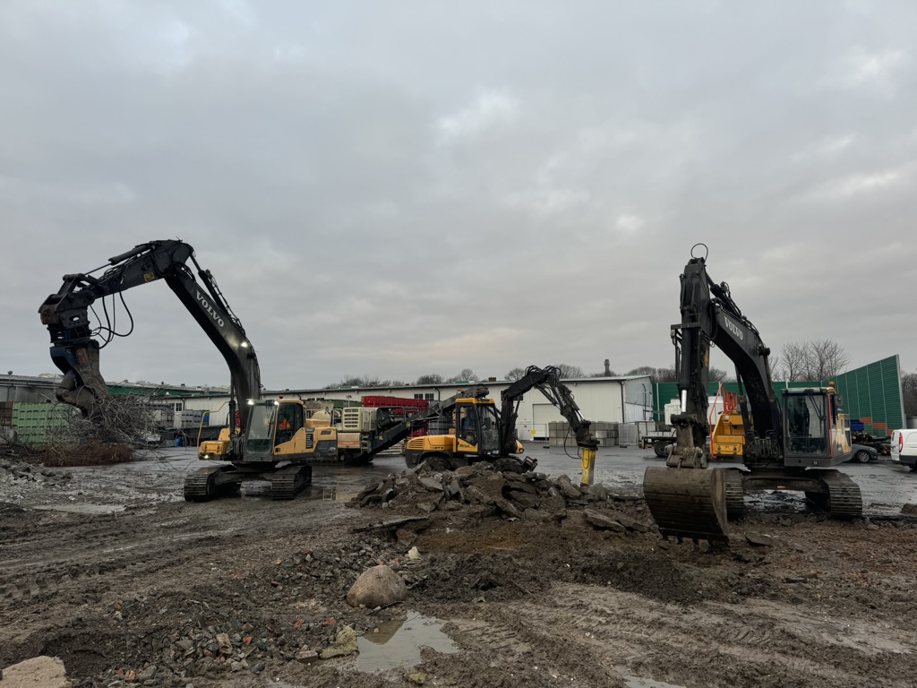 Construction site with several Volvo excavators and piles of dirt and rubble under a cloudy sky.