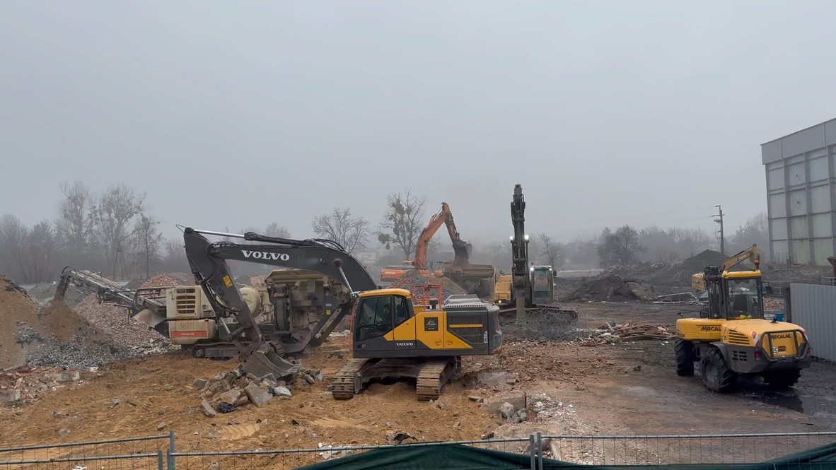 Construction site with multiple excavators clearing dirt and debris under a gray sky.