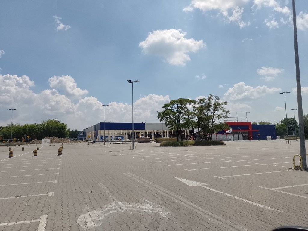 Empty parking lot in front of a blue and red building under a cloudy sky with trees near the building.