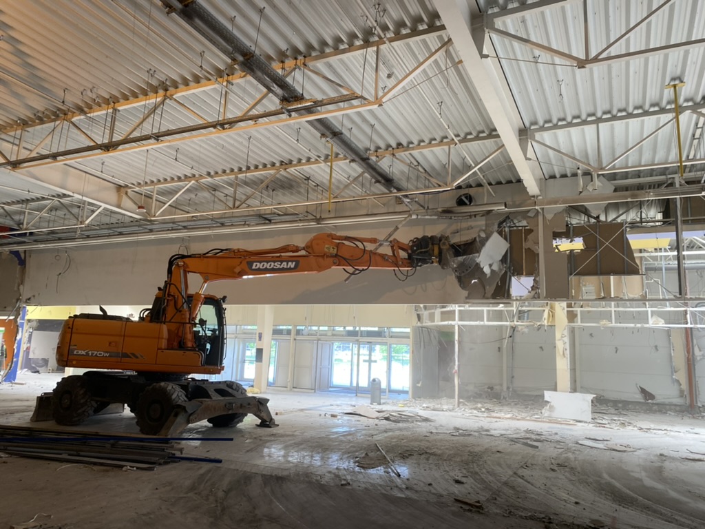 Orange Doosan excavator demolishing interior wall inside large industrial building.