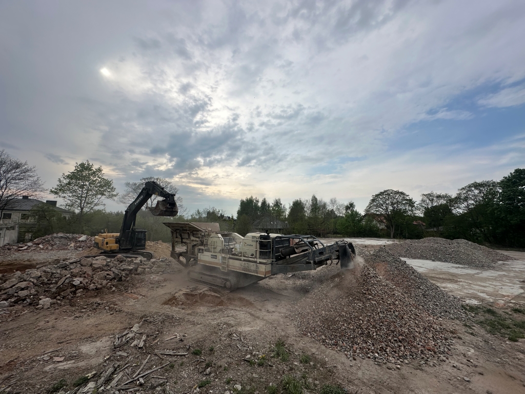 Excavator loading rocks into a crusher machine at a construction site with piles of gravel.