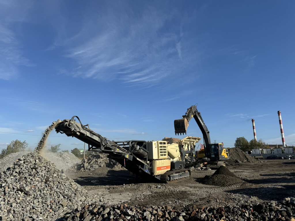 Heavy machinery crushing and piling rocks on a construction site under a blue sky.