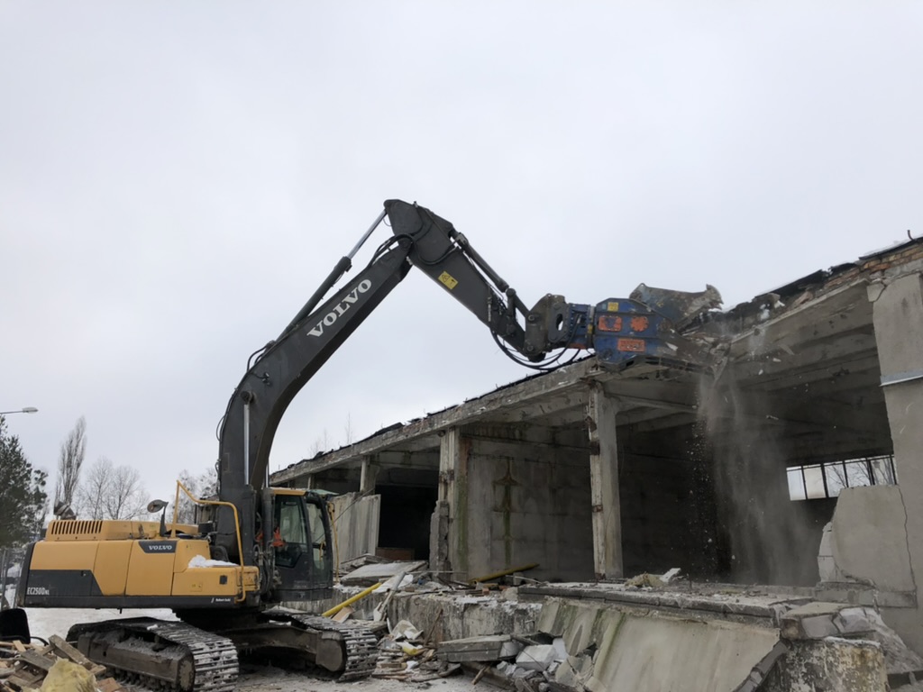 Volvo excavator demolishing a concrete building on a snowy construction site.