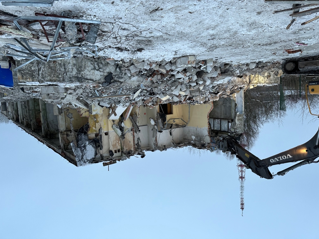 Demolition of a partially torn building with rubble and a Volvo excavator at the site.