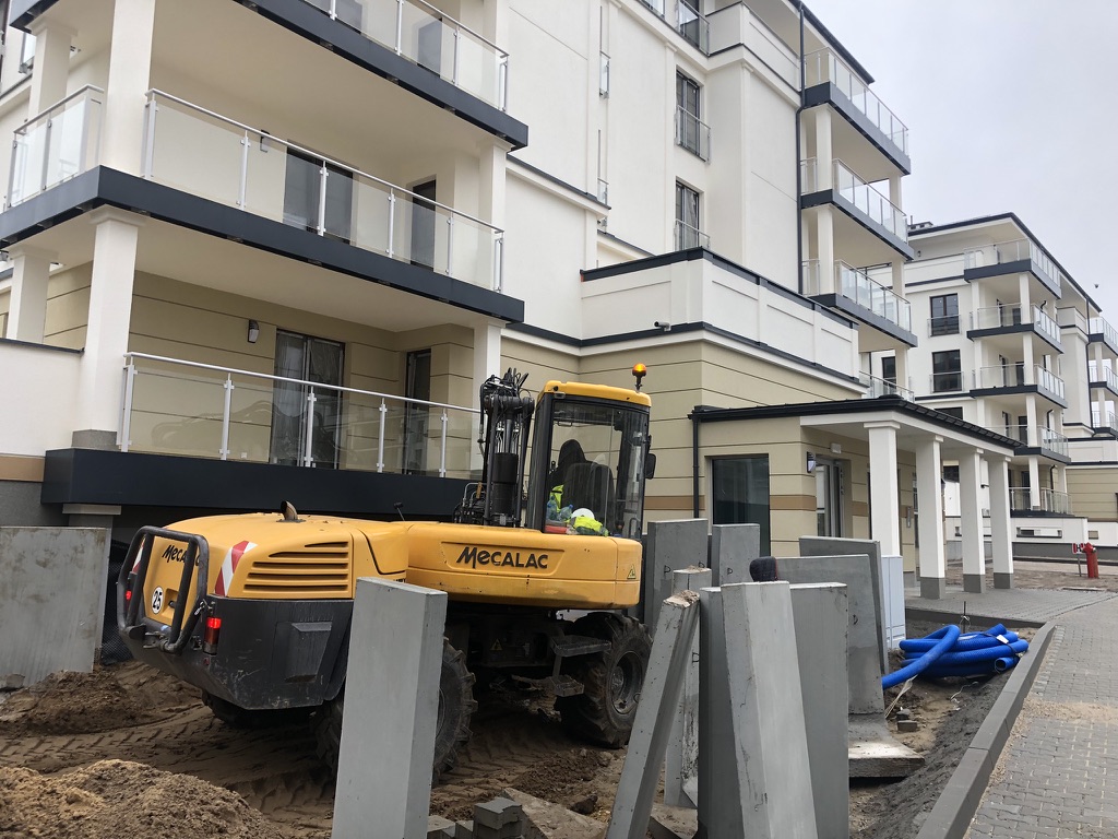 Yellow Mecalac construction vehicle at a building site next to stacked concrete slabs on a cloudy day.