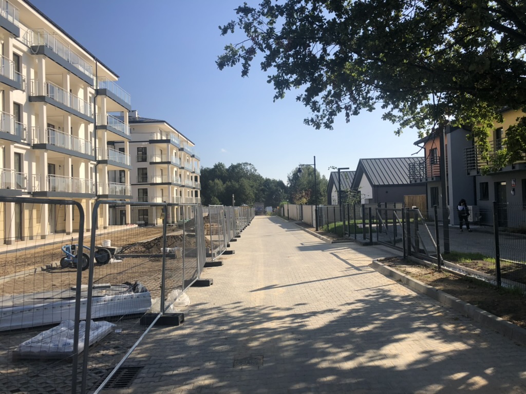 Paved street flanked by apartment buildings under construction on left and finished houses on right under a clear sky.