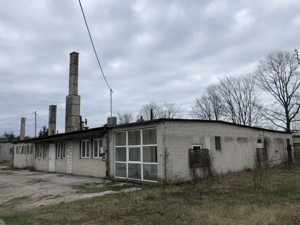 Long single-story brick industrial building with tall chimneys under a cloudy sky.