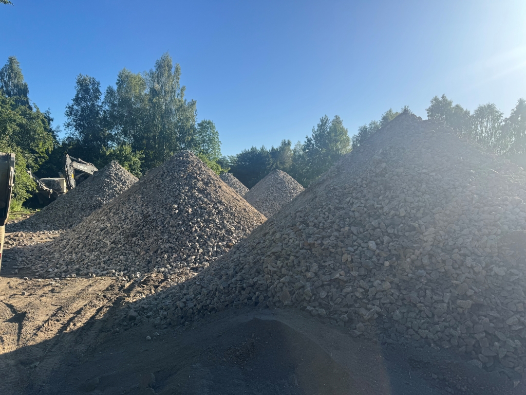Several large piles of crushed rocks at a construction site with trees and blue sky in the background.