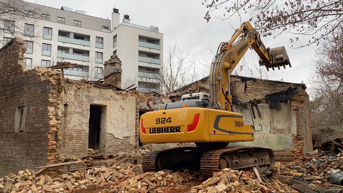 Yellow Liebherr excavator demolishing old brick building surrounded by rubble under cloudy sky.