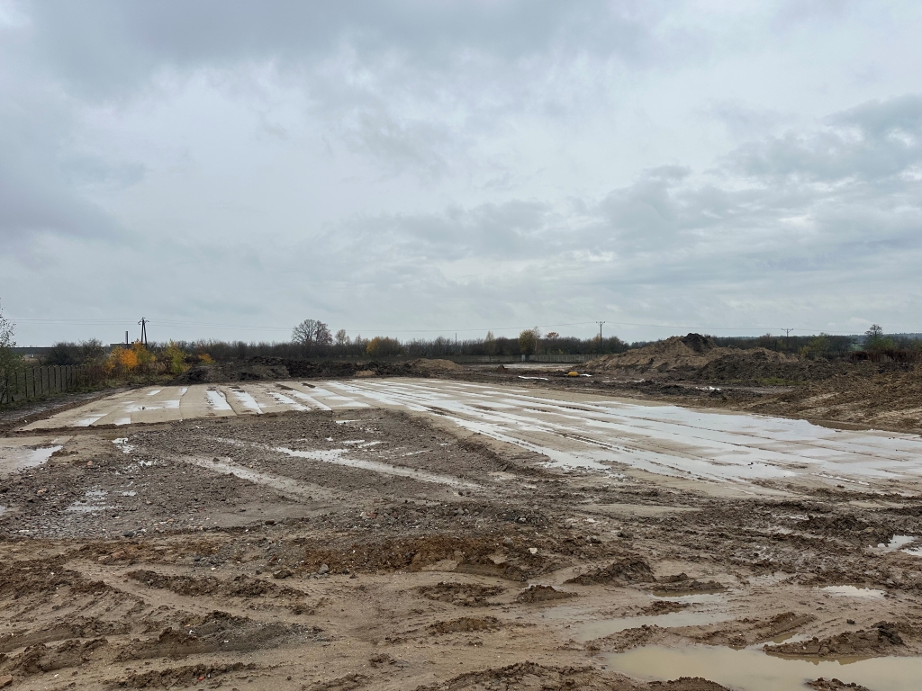 Muddy construction site with wet tire tracks, puddles, earth piles, and an overcast sky.
