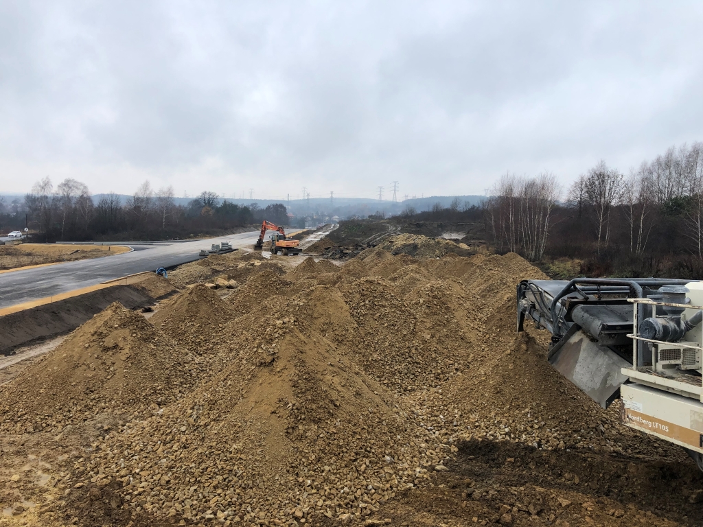 Construction site with earth piles and an orange excavator under a cloudy sky.