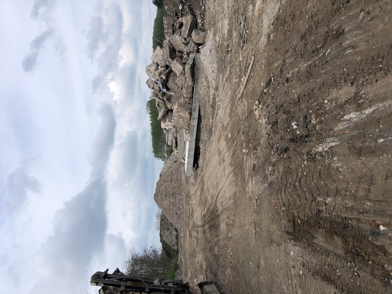 Construction site with dirt ground, heavy machinery, and piles of rubble and gravel under cloudy sky.
