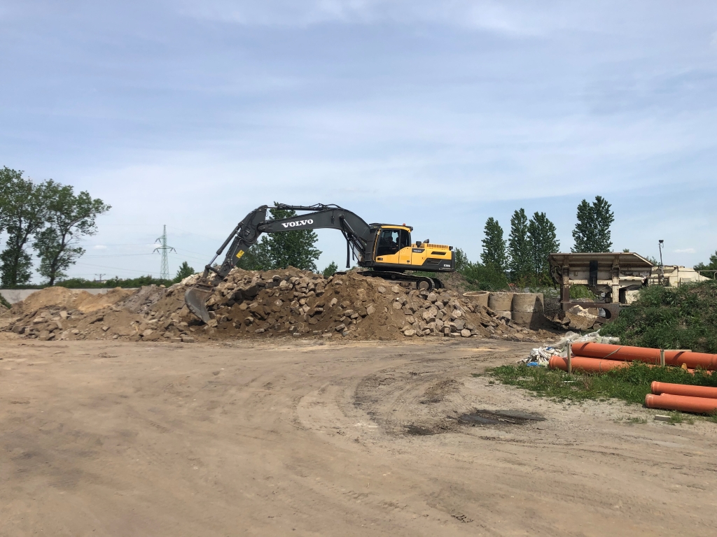 Yellow Volvo excavator on a large pile of rocks and dirt at a construction site on a clear day.