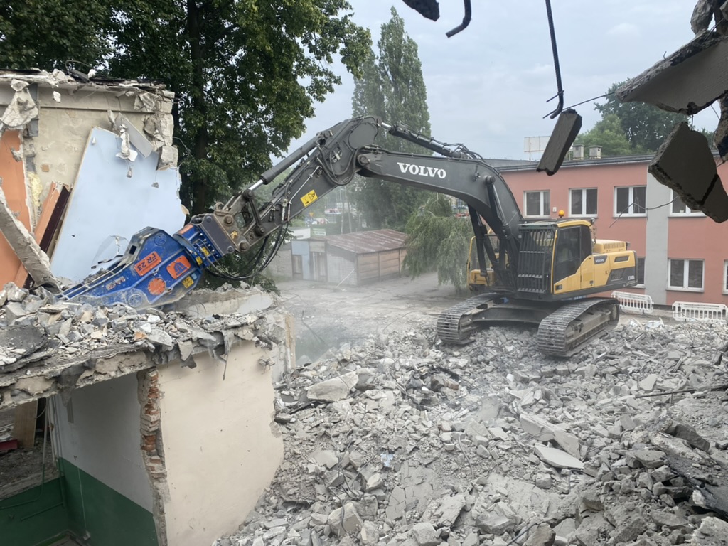 Yellow Volvo excavator demolishing a building with rubble scattered around the site.