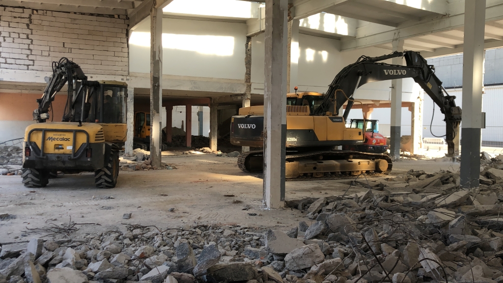 Two excavators inside a partially demolished building with rubble and debris on the floor.