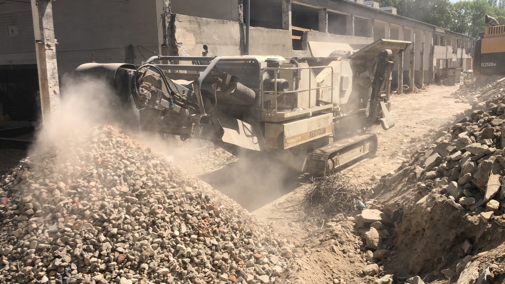 Construction site with machinery crushing concrete rubble into smaller pieces creating dust.