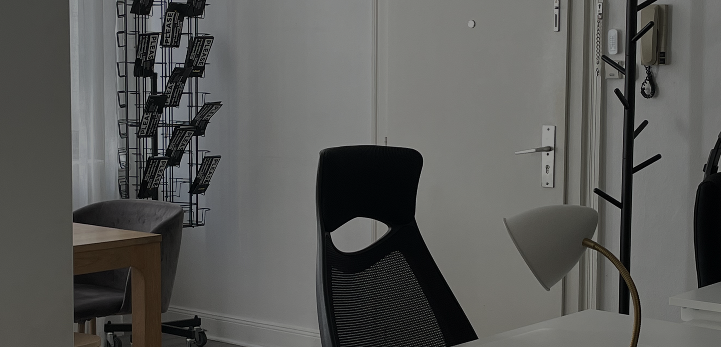 Coin bureau avec chaise noire, lampe de bureau, porte blanche, et porte-cartes sur un mur.