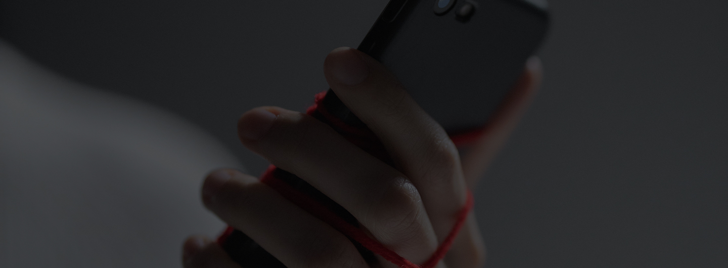 Main tenant un smartphone enveloppé d'un fil rouge dans une lumière faible.