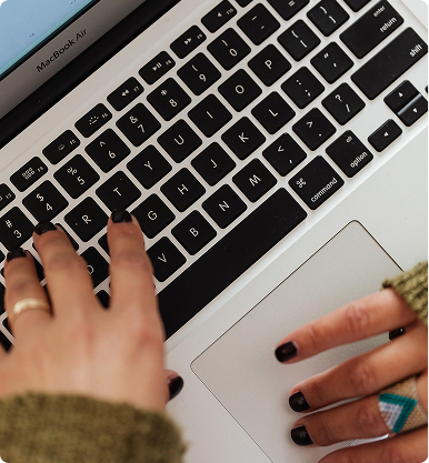 Mains avec ongles noirs tapant sur un clavier MacBook Air argenté.