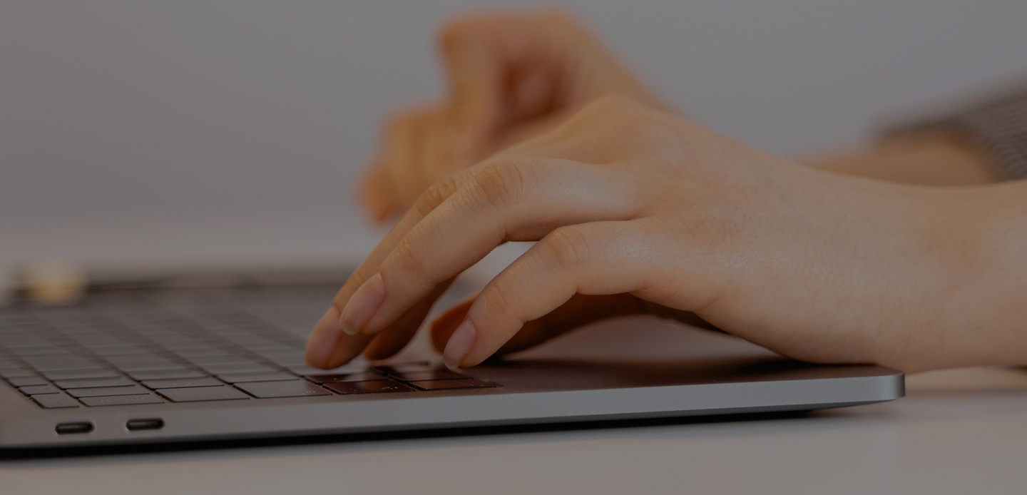Mains tapant sur le clavier d’un ordinateur portable noir sur une surface blanche.
