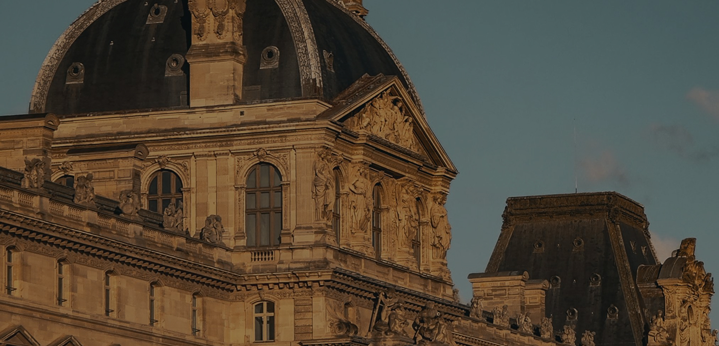 Détail architectural du Louvre à Paris, montrant des sculptures et une coupole au coucher du soleil.