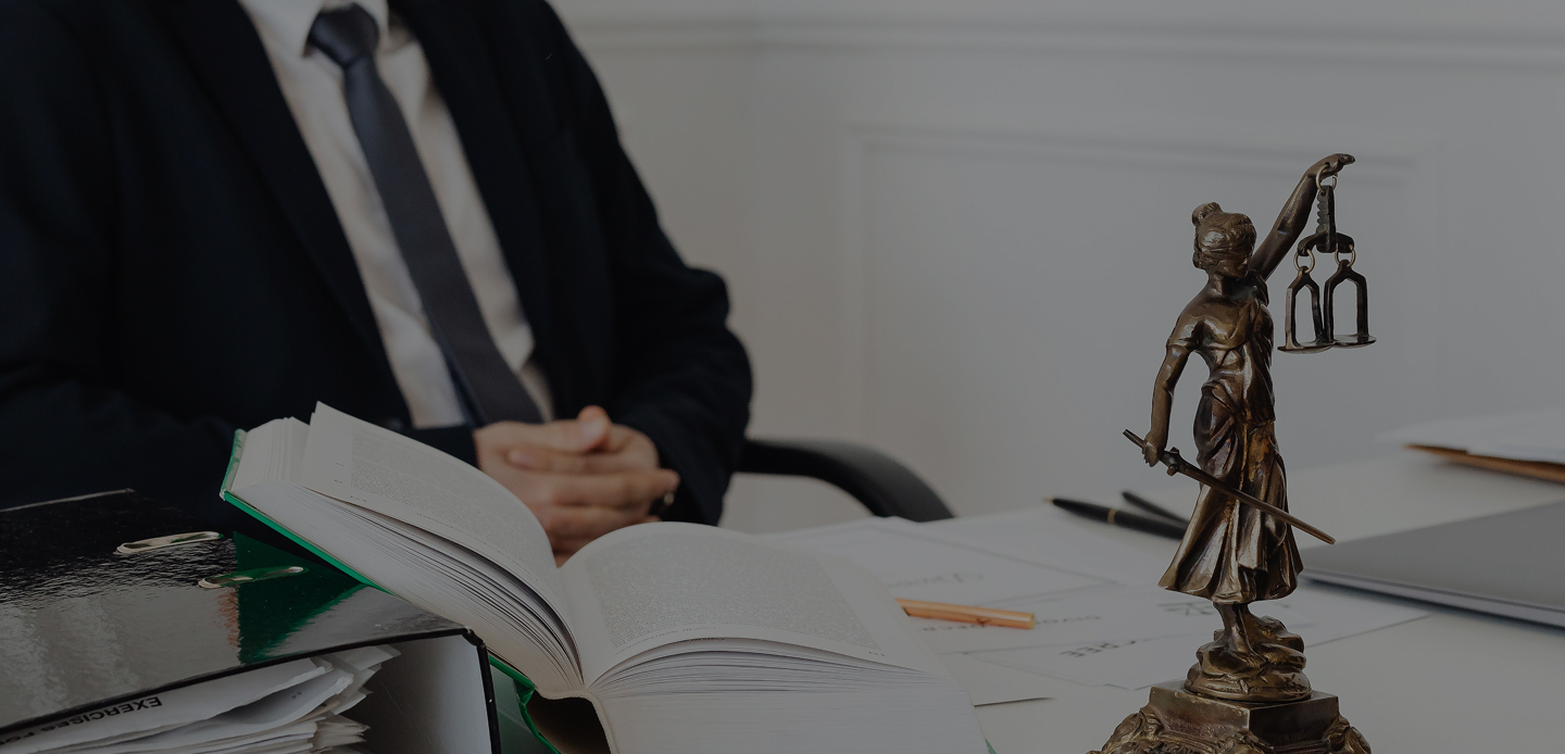 Statue de la justice avec livre ouvert, stylo et homme en costume dans un bureau.