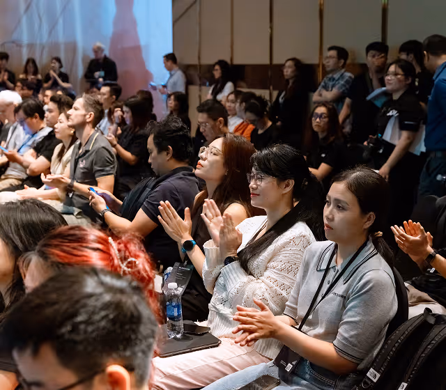 Audience of diverse people sitting and clapping at an indoor event or conference.