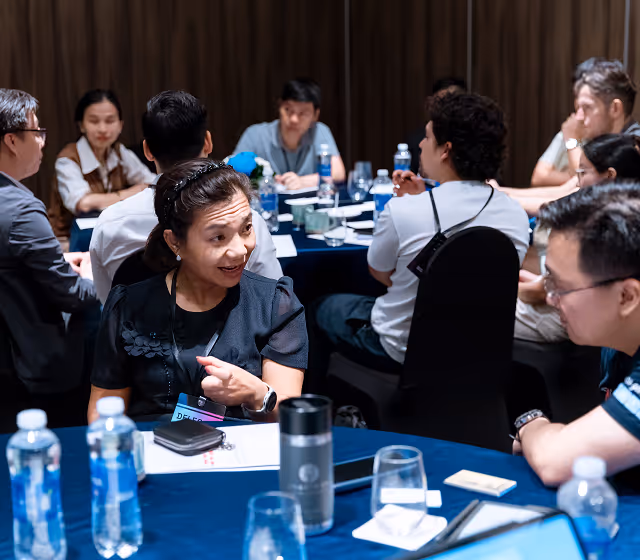 Group of people sitting around tables engaged in discussion during a meeting or conference.