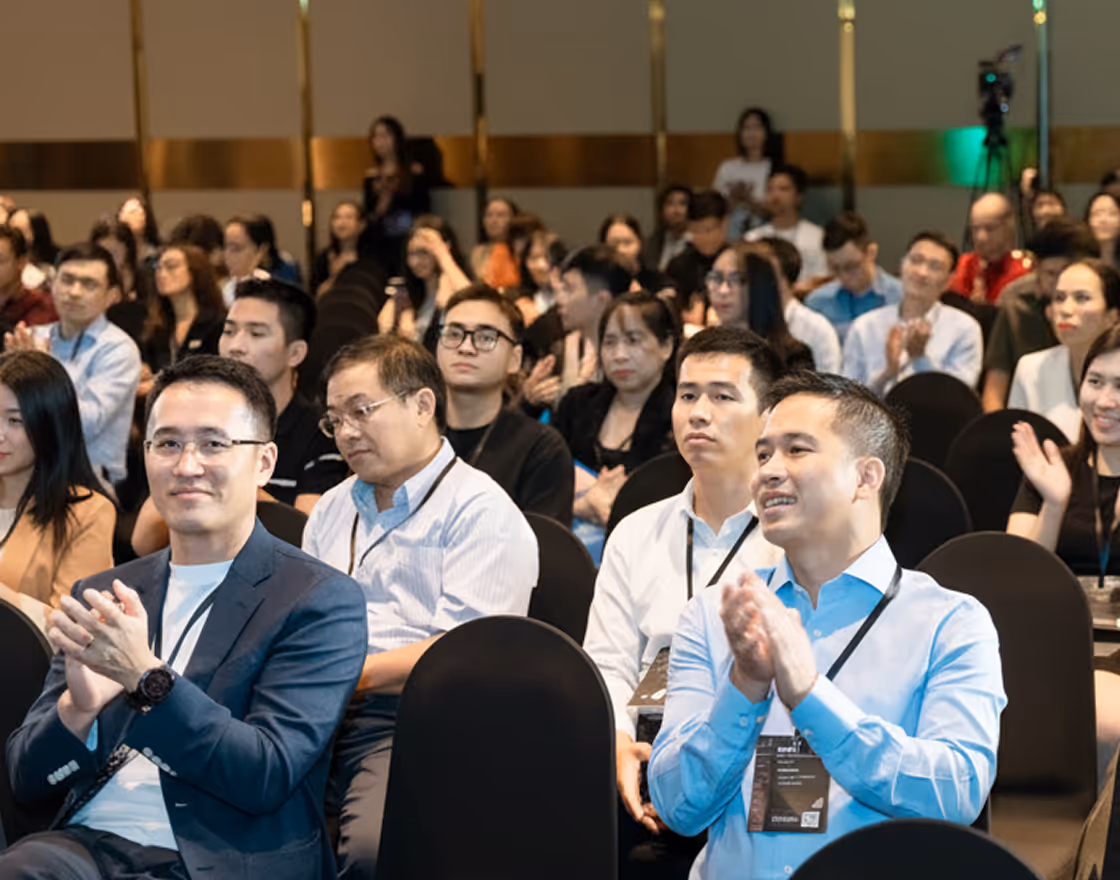 A group of men sitting around a table with blue tablecloth, engaged in discussion with water bottles and a floral centerpiece in the middle.