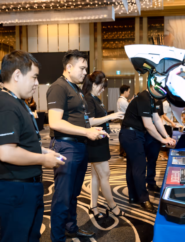 A group of people wearing black shirts and event badges interacting with electronic devices at a technology exhibition booth.