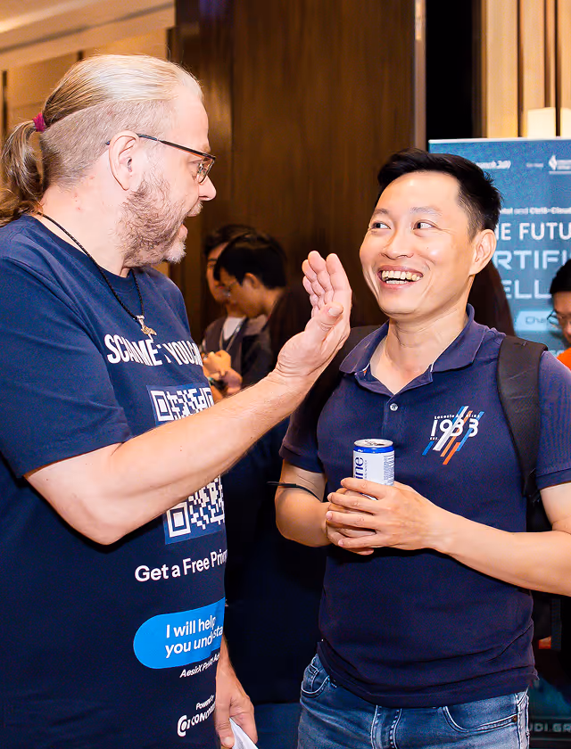 Two men engaged in friendly conversation, one smiling while holding a drink can and the other gesturing with his hand.