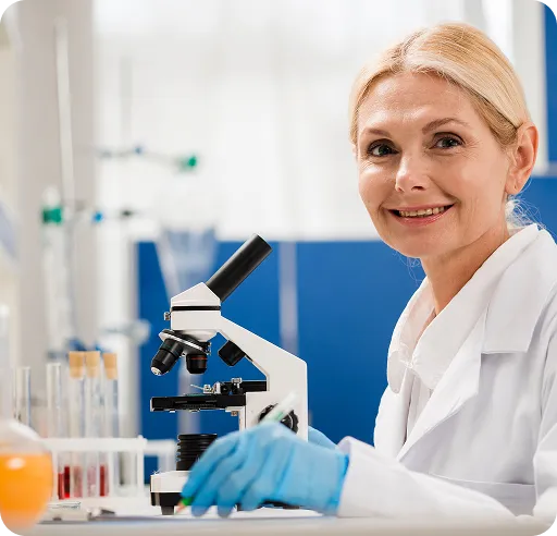 Smiling female scientist in white lab coat and blue gloves working with a microscope in a laboratory.