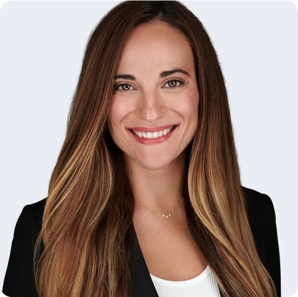 Smiling woman with long brown hair wearing a black blazer and white top against a light background.
