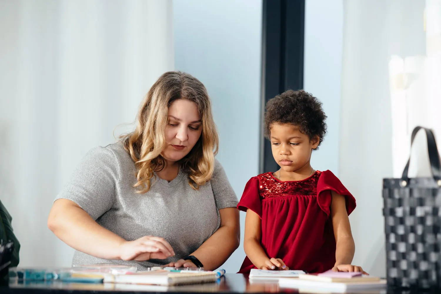Woman and young girl sitting at a table engaged in an arts and crafts activity with paper and colored materials.