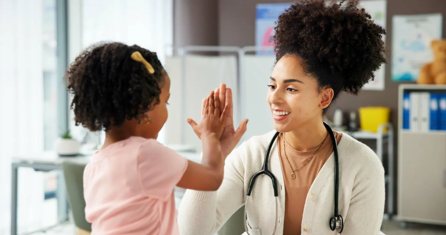 Smiling female doctor giving a high five to a young girl in a medical office.