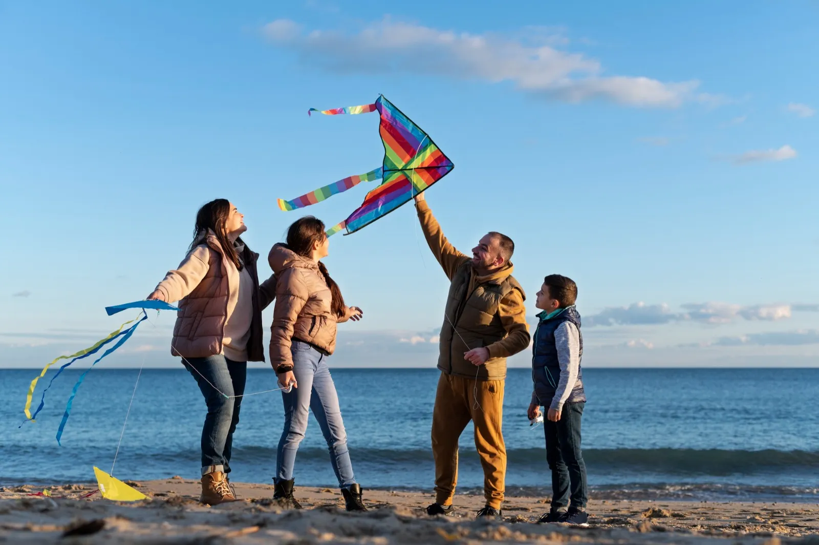 Group of people on a beach flying colorful kites under a clear blue sky.