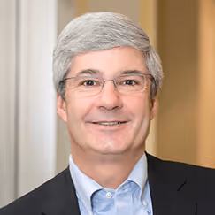 Smiling professional in glasses and suit jacket against neutral background