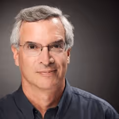 Mature professional in glasses and dark shirt against neutral background