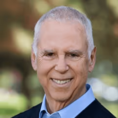 Smiling elderly man in blue shirt and dark jacket outdoors